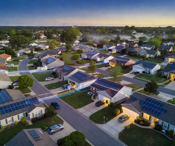 Aerial twilight view of a quiet American suburban neighborhood with glowing rooftop solar panels on dozens of homes, soft blue and gold light emanating from battery storage units visible through garage windows, interconnected by subtle glowing data lines representing a virtual power plant network, photorealistic, cinematic drone photography style, warm hopeful atmosphere, ultra high detail