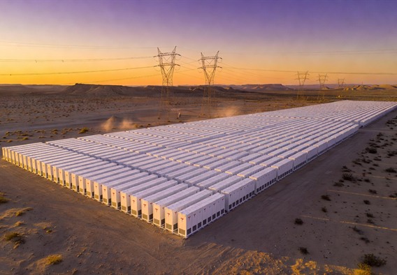 Aerial drone photograph of a vast Tesla Megapack installation stretching across a desert landscape at golden hour, rows of white battery enclosures casting long shadows, high-voltage transmission towers visible in the background against a gradient sky of deep orange and violet, photorealistic, highly detailed, cinematic lighting, ultra-wide angle