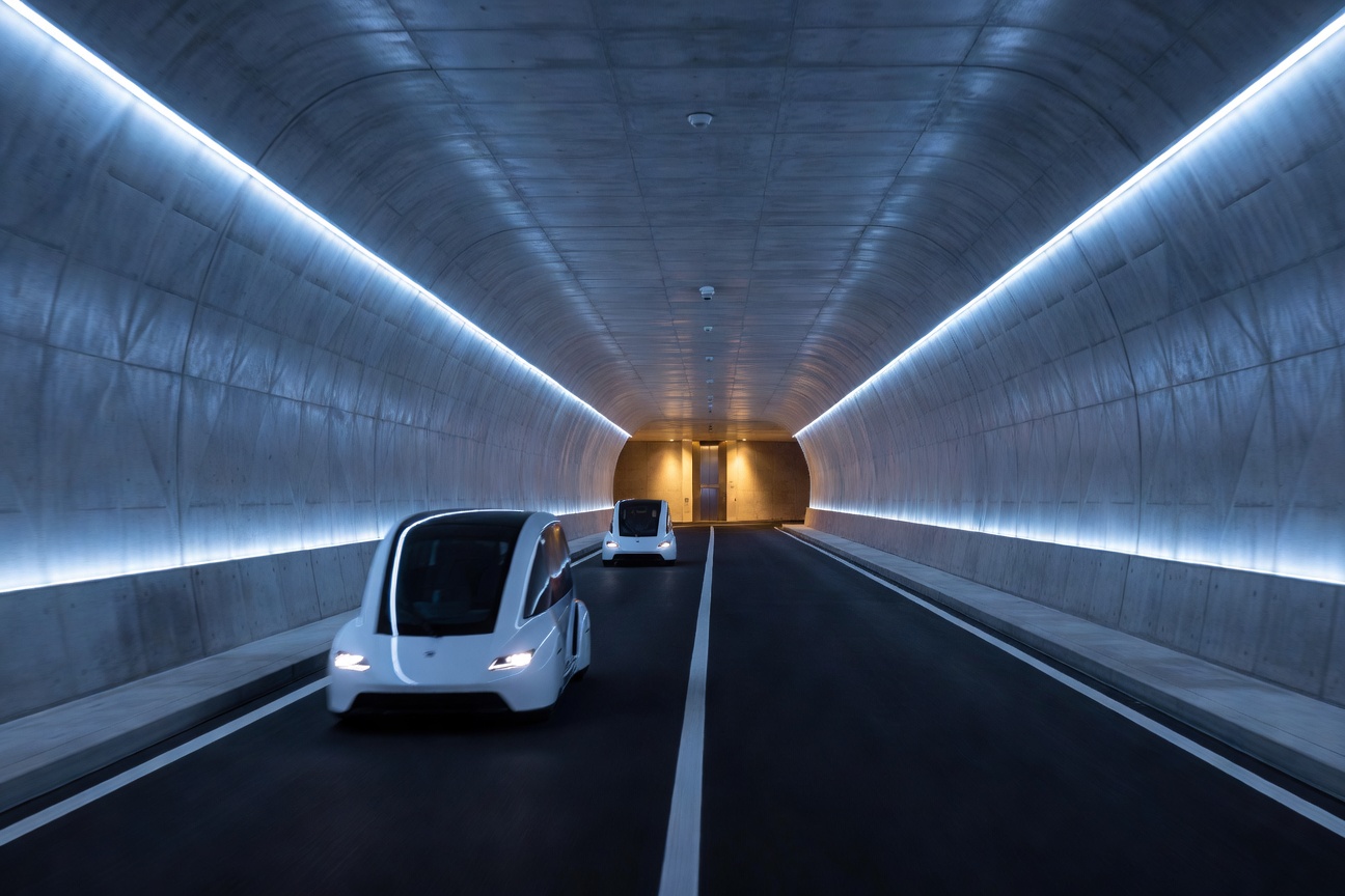 Futuristic underground tunnel illuminated with blue LED lights showing Tesla vehicles transporting passengers beneath a modern city