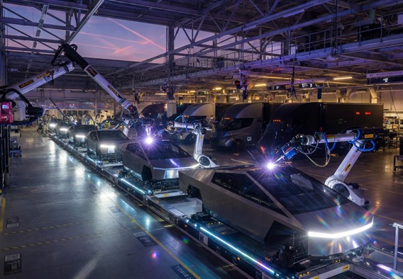 A dramatic wide-angle view of a massive futuristic Gigafactory interior at dusk, with a lineup of silver angular Cybertruck bodies and Tesla Semi trucks on an illuminated assembly line, robotic arms glowing blue-white moving in choreographed precision, lens flare catching polished stainless steel surfaces, photorealistic, cinematic lighting, ultra high detail, 8K resolution