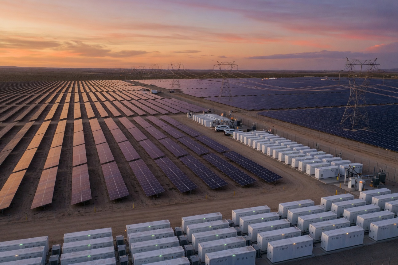 Vast solar farm connected to rows of Tesla Megapack battery storage units at dusk, glowing softly against an amber sky