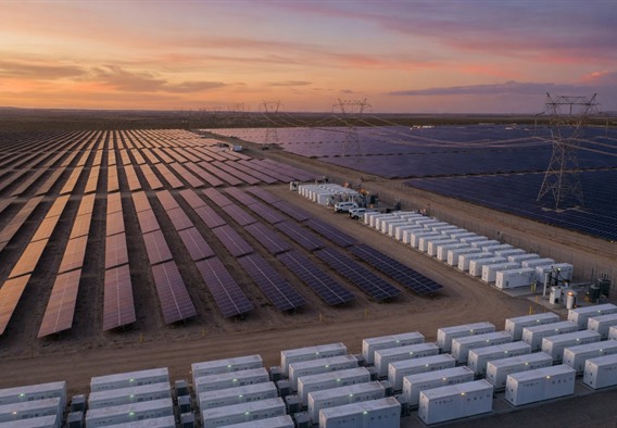 Wide aerial photorealistic render of a massive utility-scale solar farm at dusk, thousands of panels reflecting amber and violet sky, with dozens of Tesla Megapack battery storage units arranged in geometric rows along the perimeter, soft glowing indicator lights visible on each unit, transmission lines stretching to the horizon, cinematic lighting, hyper-detailed, 8K resolution, futuristic infrastructure photography style